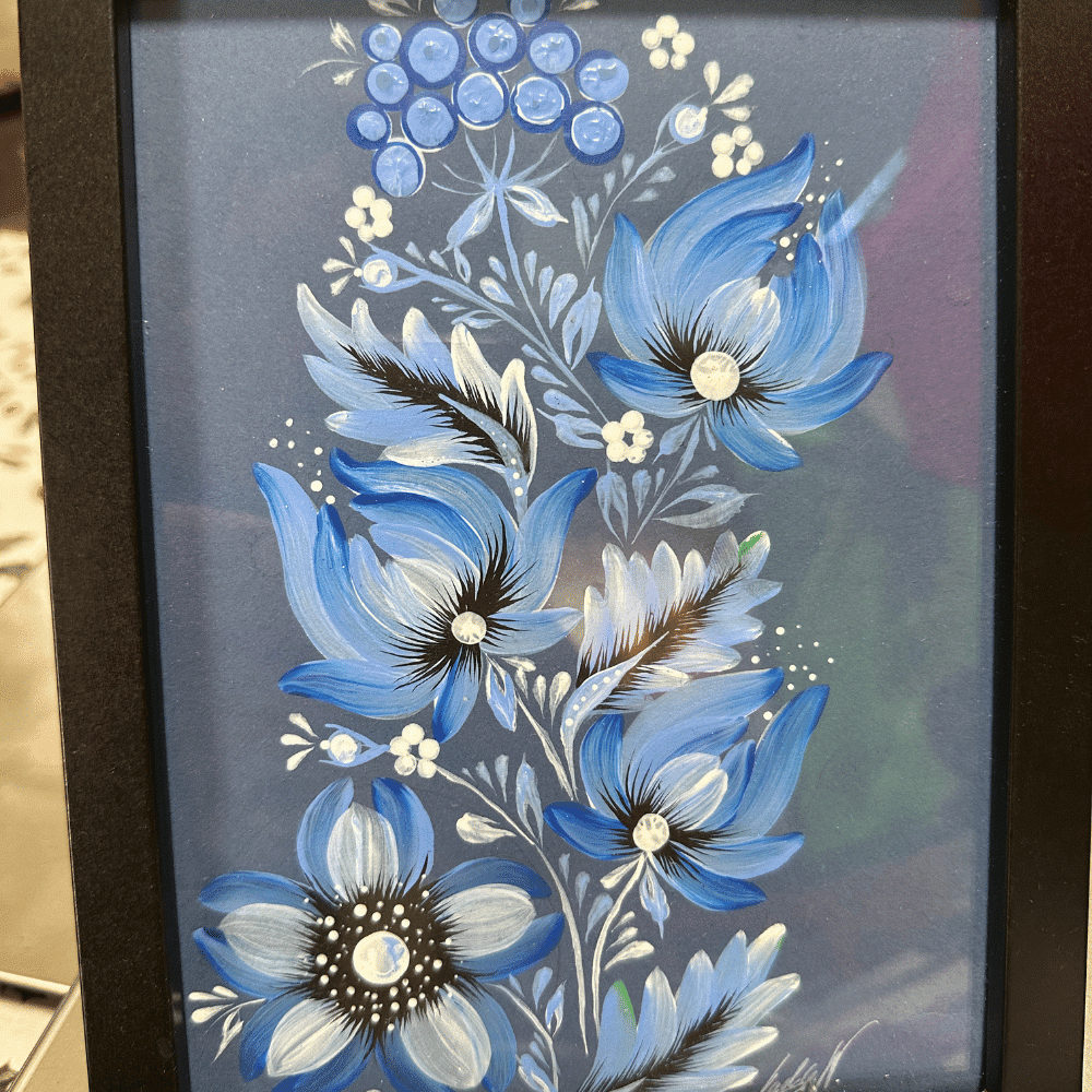 A framed painting of blue and white flowers with swirling petals and leaves, accented by clusters of round blue berries on a dark background.